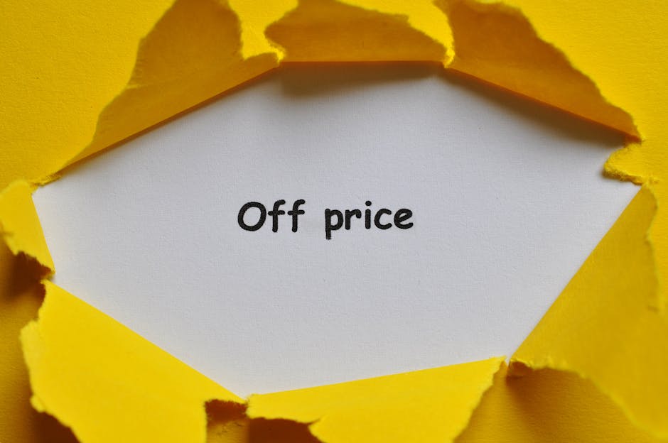 A torn yellow paper background revealing a white note inside that reads 'Off price' in black typewriter-style font. The torn edges of the paper create a rough, jagged border around the note, set against a solid yellow surface which enhances the visual focus on the message. The lighting is even, highlighting the texture of the torn paper and the clarity of the text, embodying a theme of highlighting discounts or reduced prices, relevant for domestic or commercial surface cleaning promotions. The overall composition conveys an emphasis on savings or special offers, suitable for content about affordable cleaning services offered by Colliers Wood Carpet Cleaning.